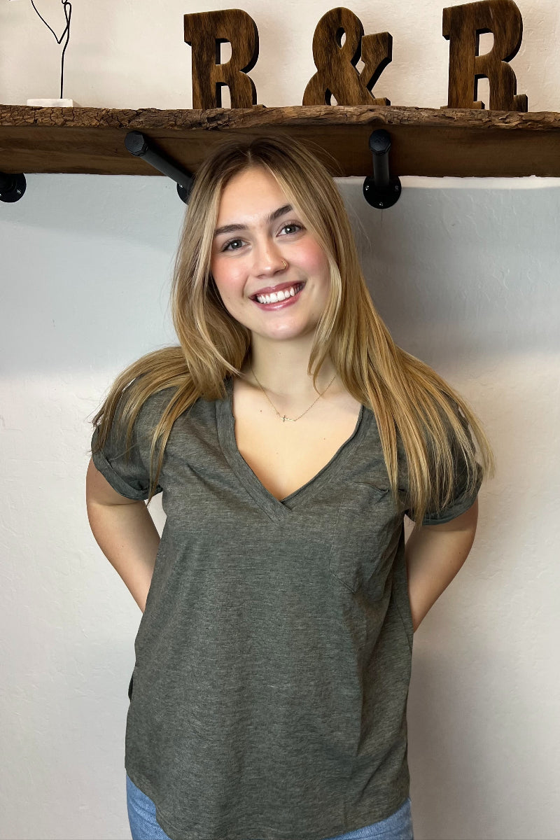 Woman wearing a green shirt and blue jeans standing in front of a wooden shelf with decorative items.