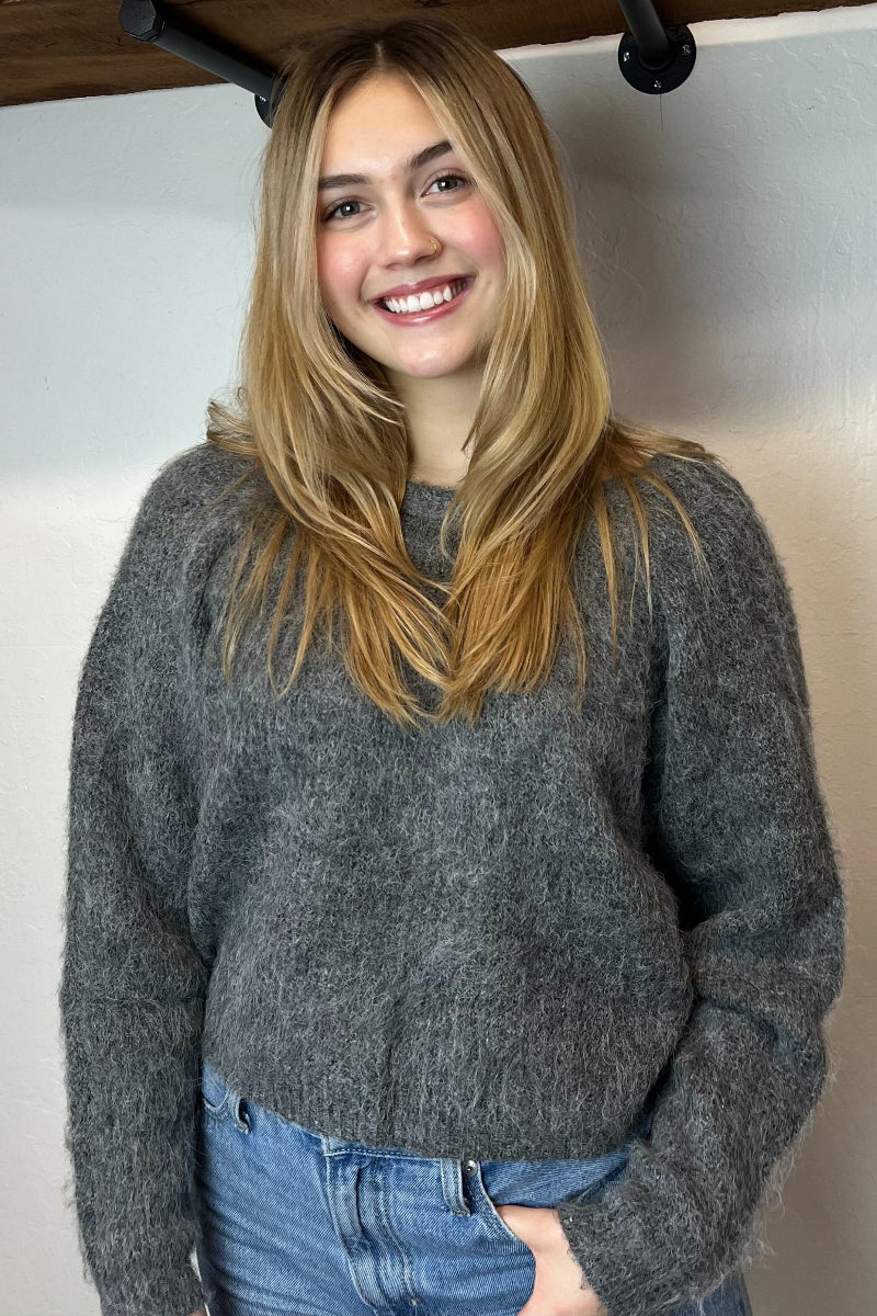 Person wearing a gray sweater and blue jeans standing against a plain background