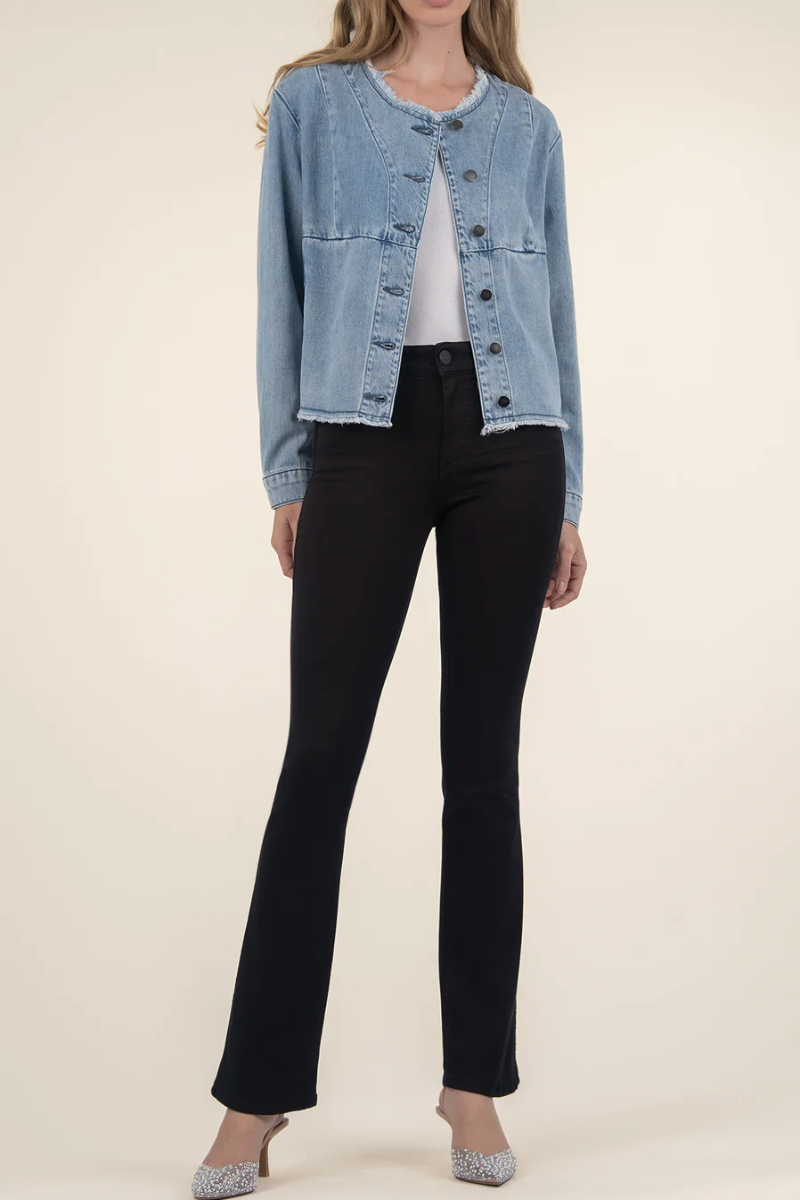 Woman wearing a light blue denim jacket over a white top and black pants on a beige background