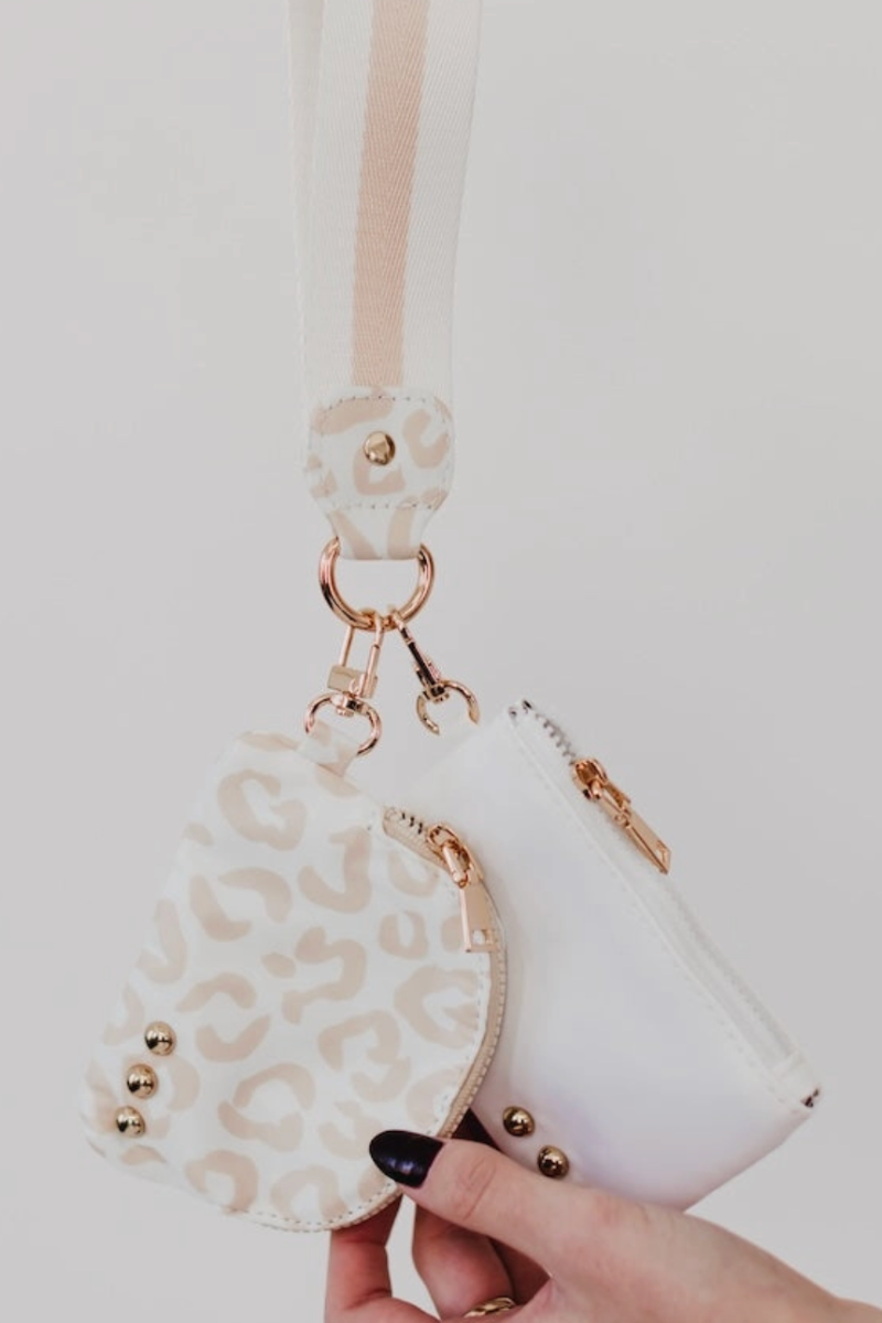 White handbag with leopard print strap held by a hand against a white background