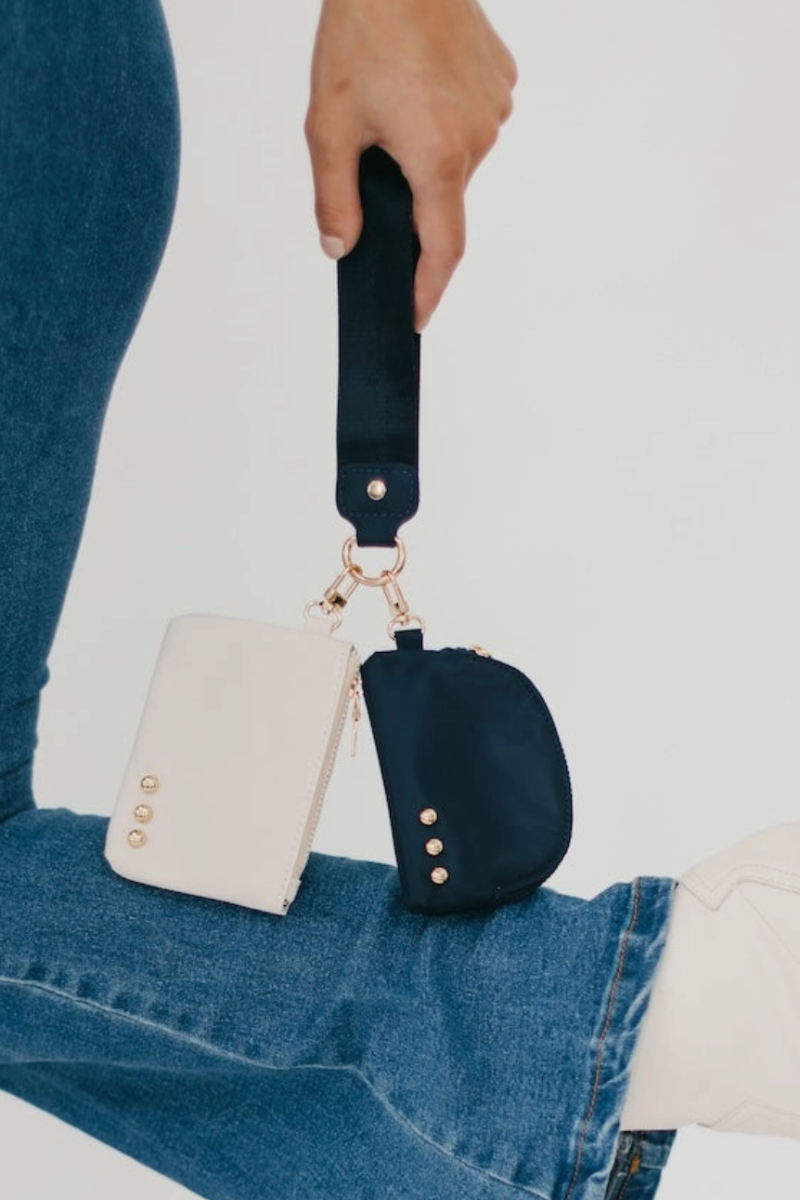 Navy blue pouch with gold accents held by a person wearing blue jeans on a white background