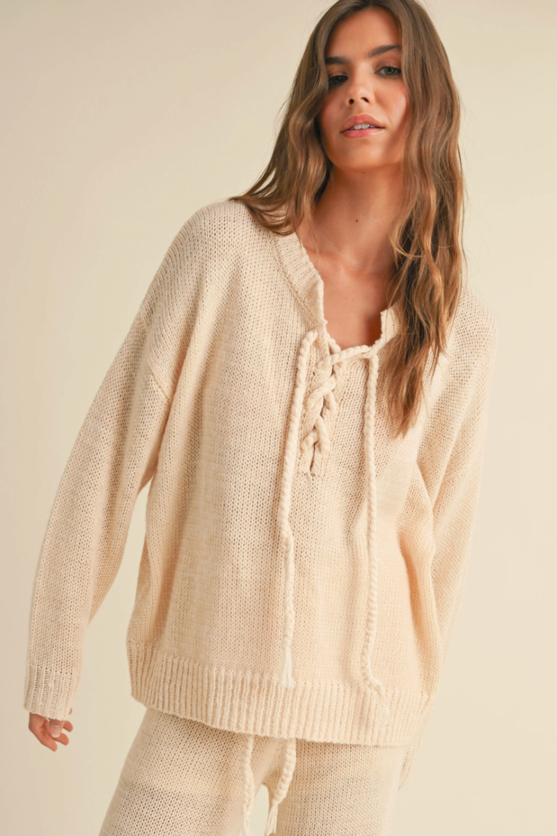 Woman wearing a beige lace-up sweater against a neutral background