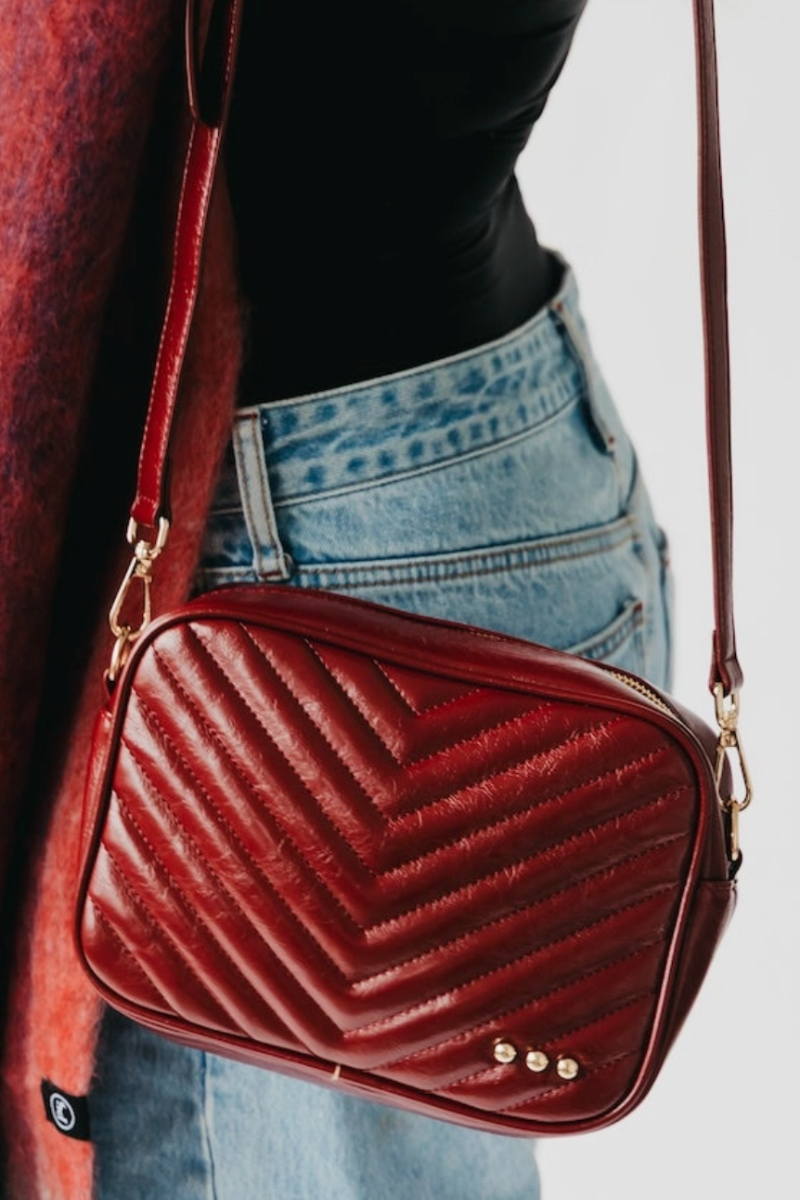 Red textured handbag with gold accents worn by a person against a neutral background