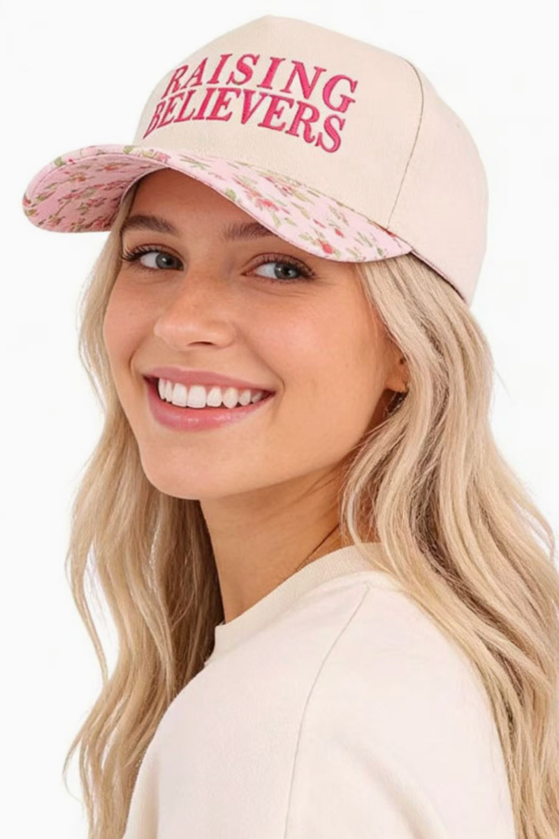 Woman wearing a beige cap with 'RAISING BELIEVERS' text on a white background