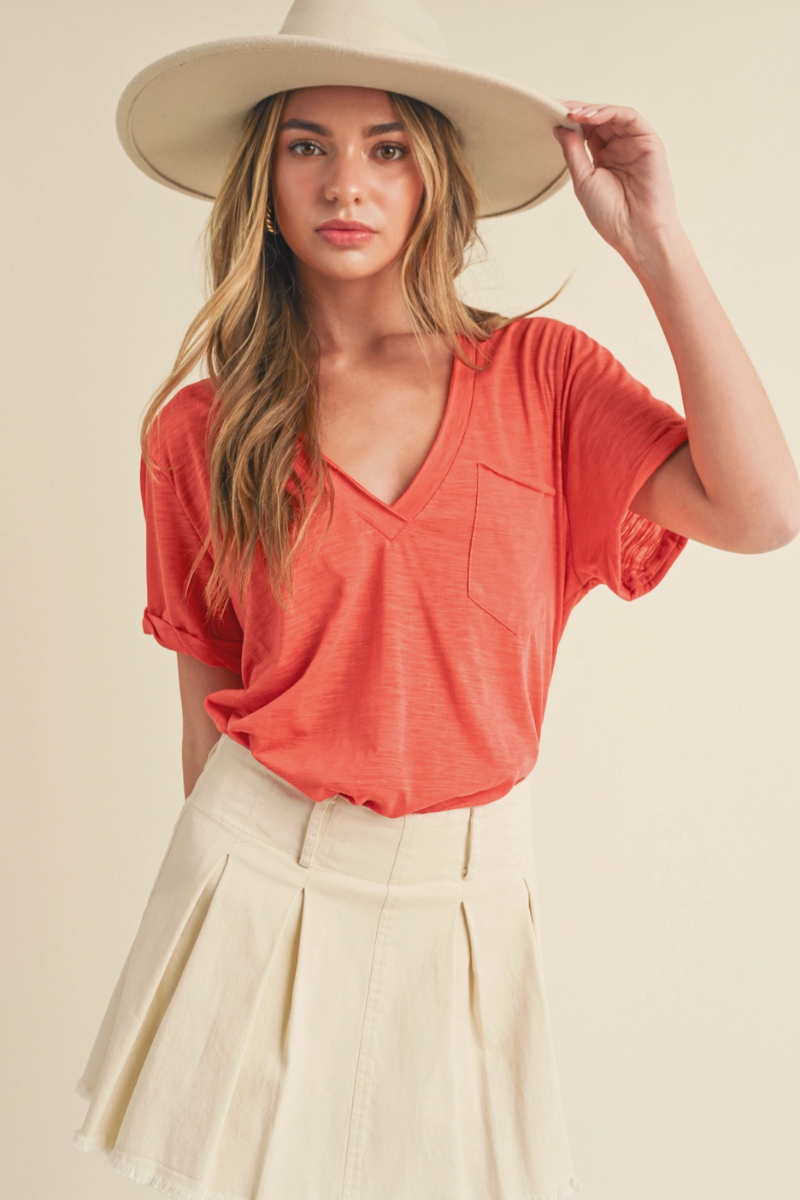 Woman wearing a coral v neck tee and beige hat against a plain background