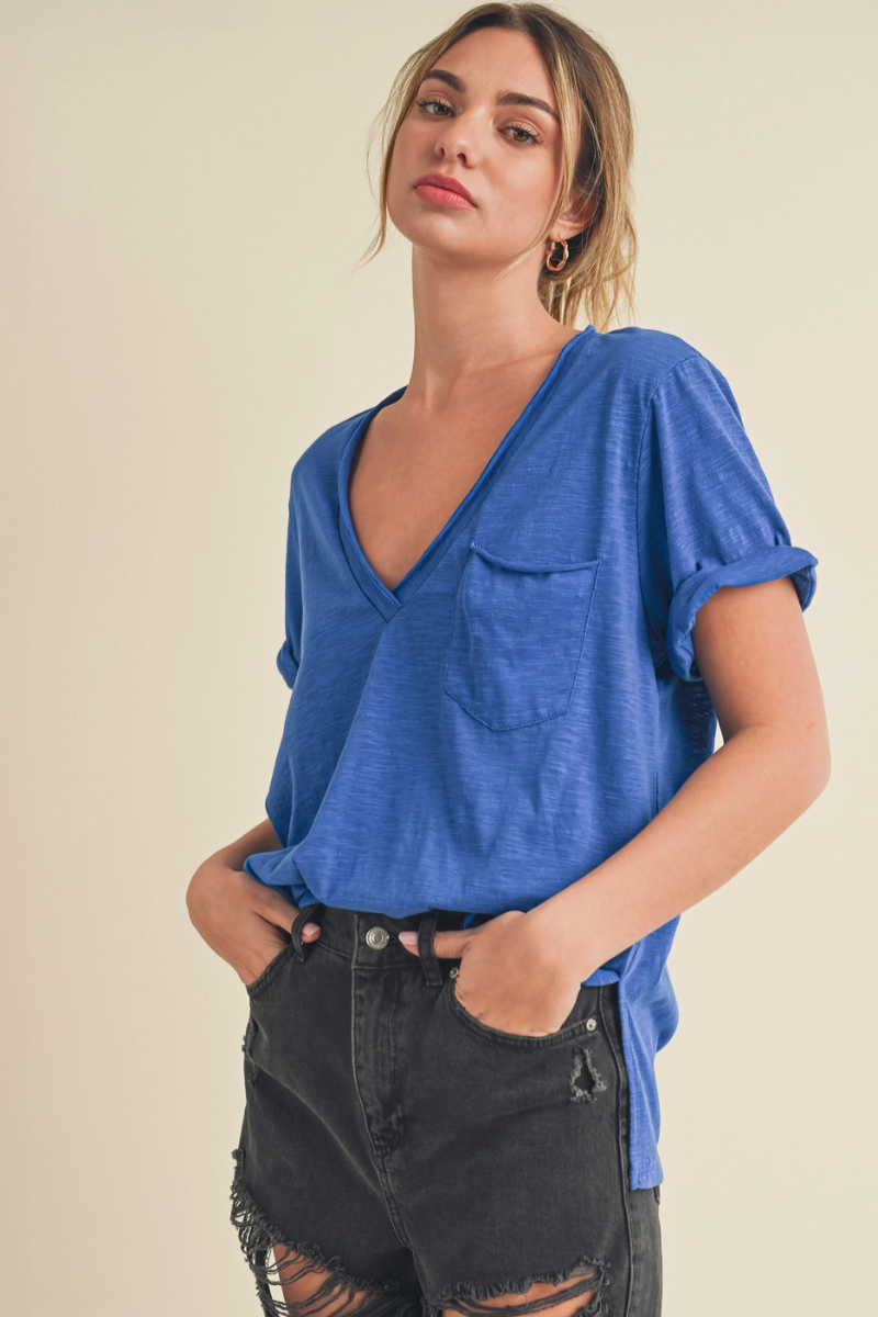 Woman wearing a blue v neck tee shirt and black pants against a beige background