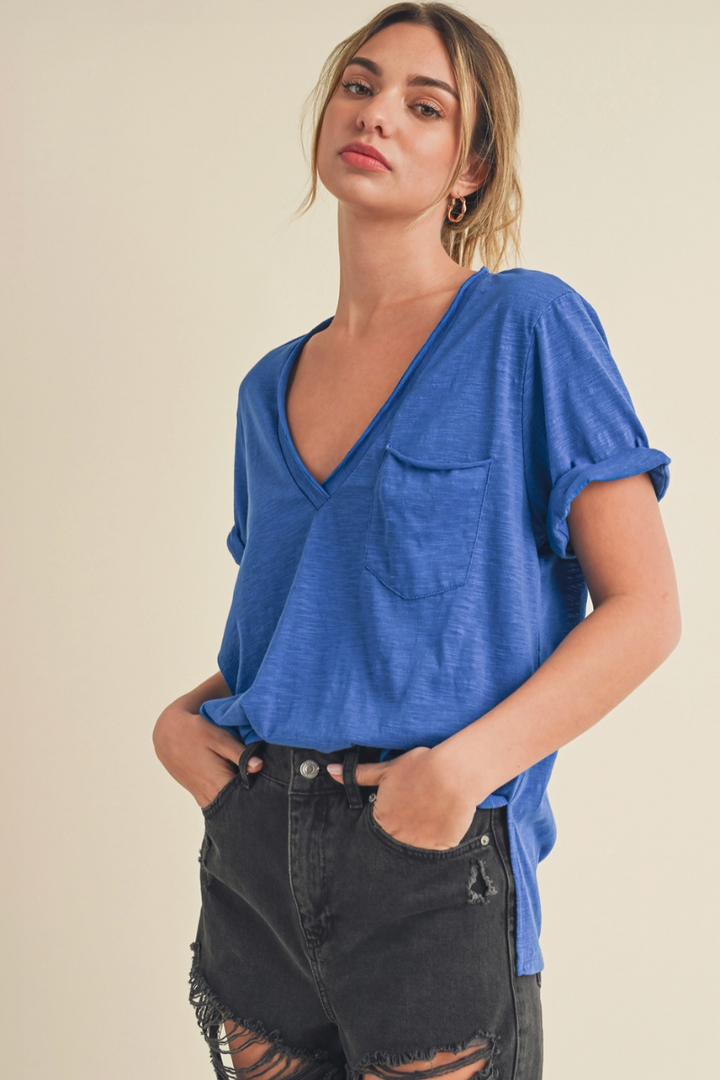 Woman wearing a blue v neck tee shirt and black pants against a beige background