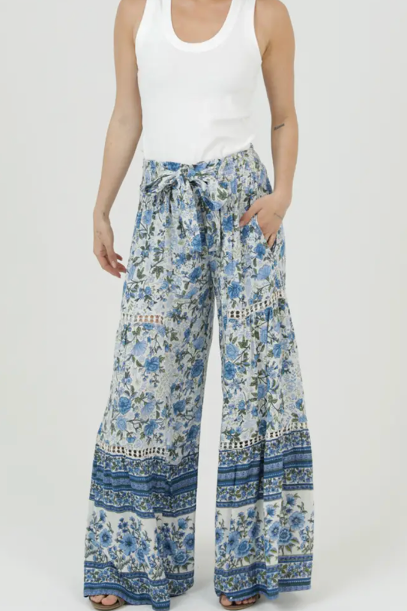 Woman wearing a white tank top and blue floral wide-leg pants on a white background