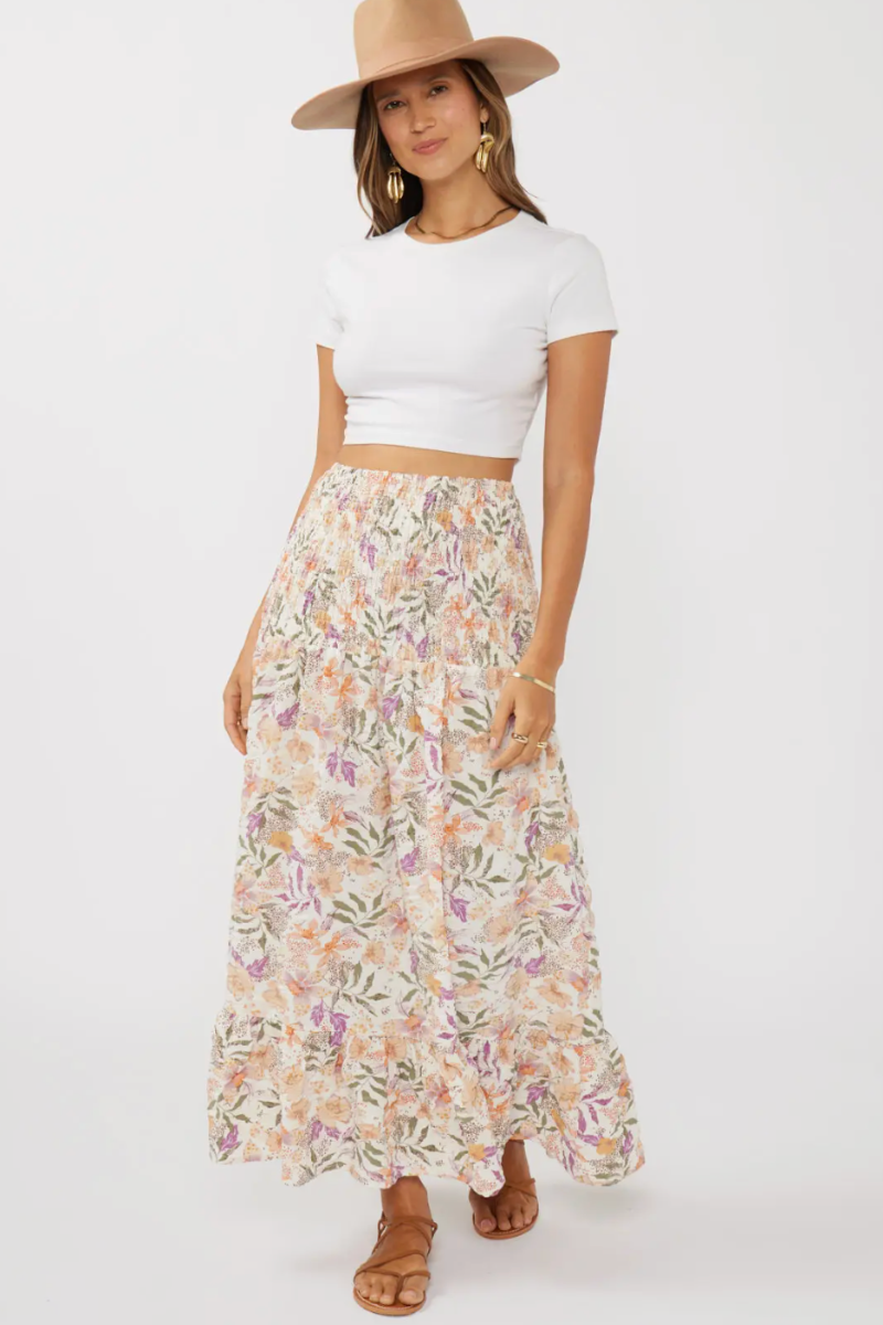 Woman wearing a white crop top and floral skirt with a beige hat on a white background